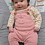 baby, infant, smiling, pink_onesie, hair_clip, flower, baby_seat, cushion, patterned, socks, cute, child, portrait, indoor, happy, small_hands, dark_hair, button, fabric, face
