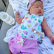 Emma is registered to the contest to win money with this photo: baby, infant, sleeping, headband, bow, purple_shorts, blanket, pacifier, bottle, outdoor, cute, peaceful, clothing, person, resting, soft_toys, newborn, infant_fashion, baby_accessories, relaxation