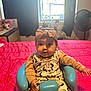 baby, child, bow_headband, mickey_mouse, onesie, baby_seat, blue_seat, red_bedspread, bedroom, window, curtains, indoor, furniture, plant, fan, table, cute, infant, smiling, seated