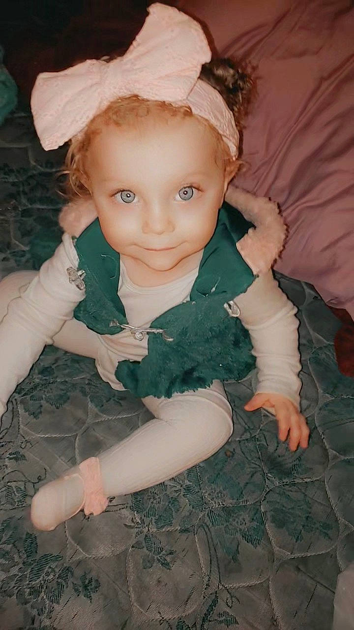 Elena is registered to the contest to win money with this photo: arm, baby_toddler_clothing, cheek, doll, eye, eyelash, fawn, grass, hand, head, headgear, headpiece, iris, joy, leg, pattern, person, pink, sitting, skin