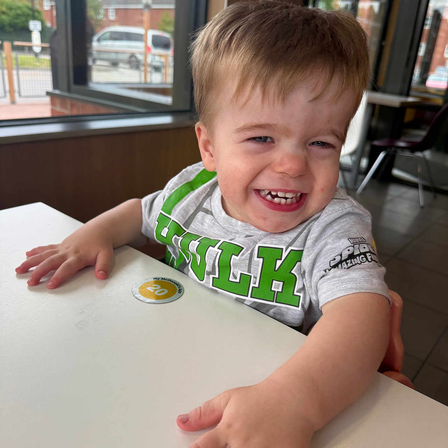 Luca is registered to the contest to win money with this photo: casual, child, clothing, daylight, expression, face, hands, happy, indoor, person, restaurant, seat, shirt, short_hair, skin, smiling, table, toddler, window, young