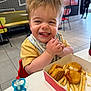 background_people, casual_dining, chair, chicken_nuggets, child, face, floor_tiles, food, french_fries, hands, happy, high_chair, indoor, pacifier, restaurant, smiling, table, toddler, window, yellow_shirt