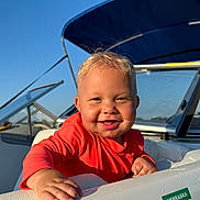 Wesley joined the competition — help win amazing prizes! baby, child, smiling, boat, watercraft, outdoor, sunlight, red_clothing, blonde_hair, blue_sky, canopy, happy, person, portrait, daytime, vacation, recreation, water, leisure, face
