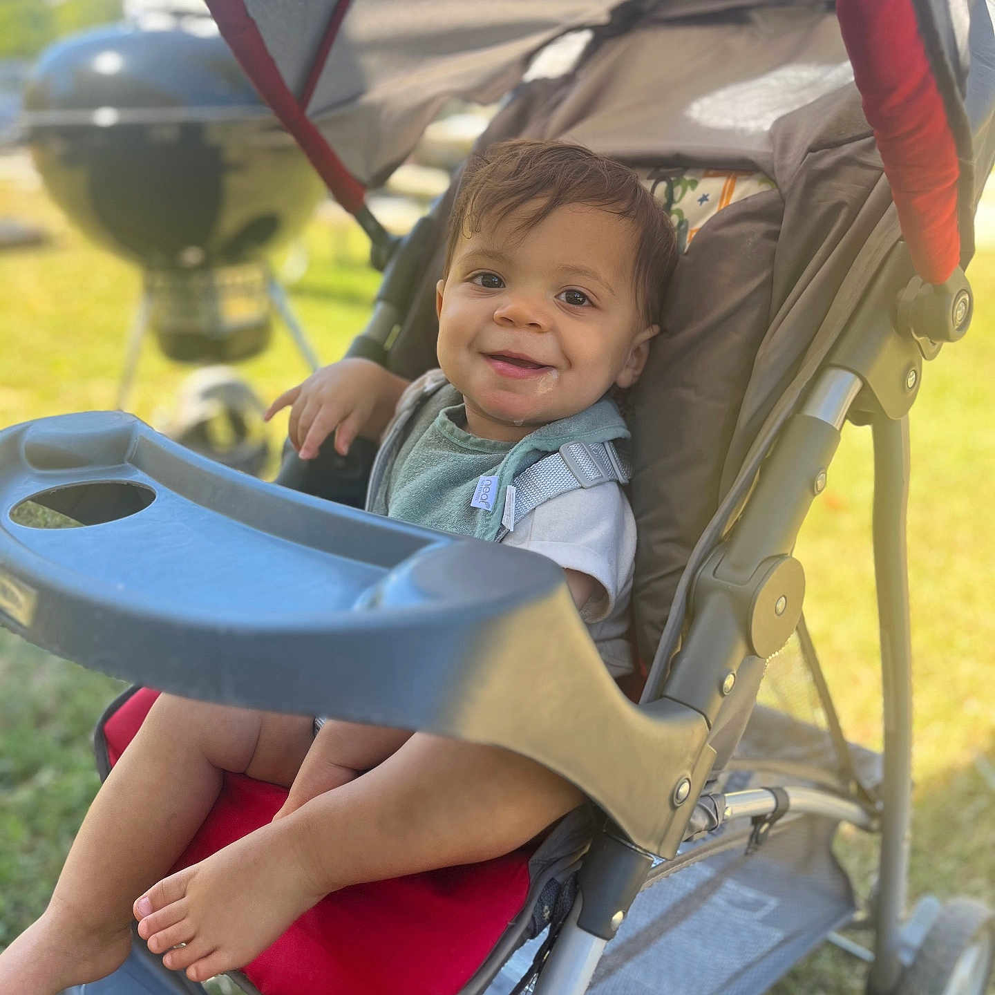 Kashton is registered to the contest to win money with this photo: baby, casual, child, daytime, face, foot, grass, happy, metal, outdoor, park, plastic, playful, red, seat, smiling, stroller, summer, sunlight, toddler