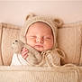 baby, sleeping, knit_hat, teddy_bear, blanket, pillow, cozy, soft_texture, infant, cute, wrapped, peaceful, child, indoors, portrait, warm_colors, newborn, hand, face, resting