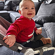 Léo a rejoint le concours — aidez-le/la à gagner de superbes lots ! baby, child, infant, smiling, red_sweater, bouncer, baby_seat, living_room, sofa, cushion, cozy, happy, portrait, indoor, hand, sock, footwear, seat_belt, natural_light, cute