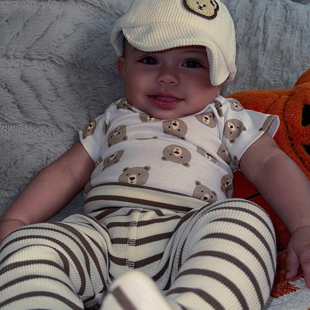 Xavier joined the competition — help win amazing prizes! baby, child, smiling, hat, bear_pattern, striped_pants, cozy, blanket, cute, indoors, portrait, infant, clothing, happy, sitting, soft_texture, cute_outfit, person, warm, playful