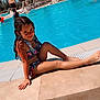 child, girl, swimsuit, pool, water, sunny, outdoor, smile, wet_hair, palm_trees, vacation, relaxing, summer, blue_sky, sunshine, lounge_chairs, umbrella, holiday, playful, happy