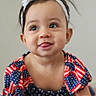 baby, child, crawling, headband, flower, patriotic, dress, stars, stripes, carpet, tongue_out, cute, smiling, indoor, person, infant, portrait, happy, young_child, neutral_background