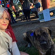 Buddy is registered to the contest to win money with this photo: woman, dog, selfie, outdoor, picnic, park, grass, brindle_dog, headband, long_hair, white_clothing, people, picnic_table, shelter, daylight, casual, leash, fun, gathering, smile