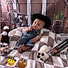 baby, cowboy_hat, plush_toy, blanket, denim_overalls, cute, indoors, child, western_theme, cowboy, hat, soft_toy, checkered_blanket, decor, background, baby_boy, face, portrait, sitting, playful