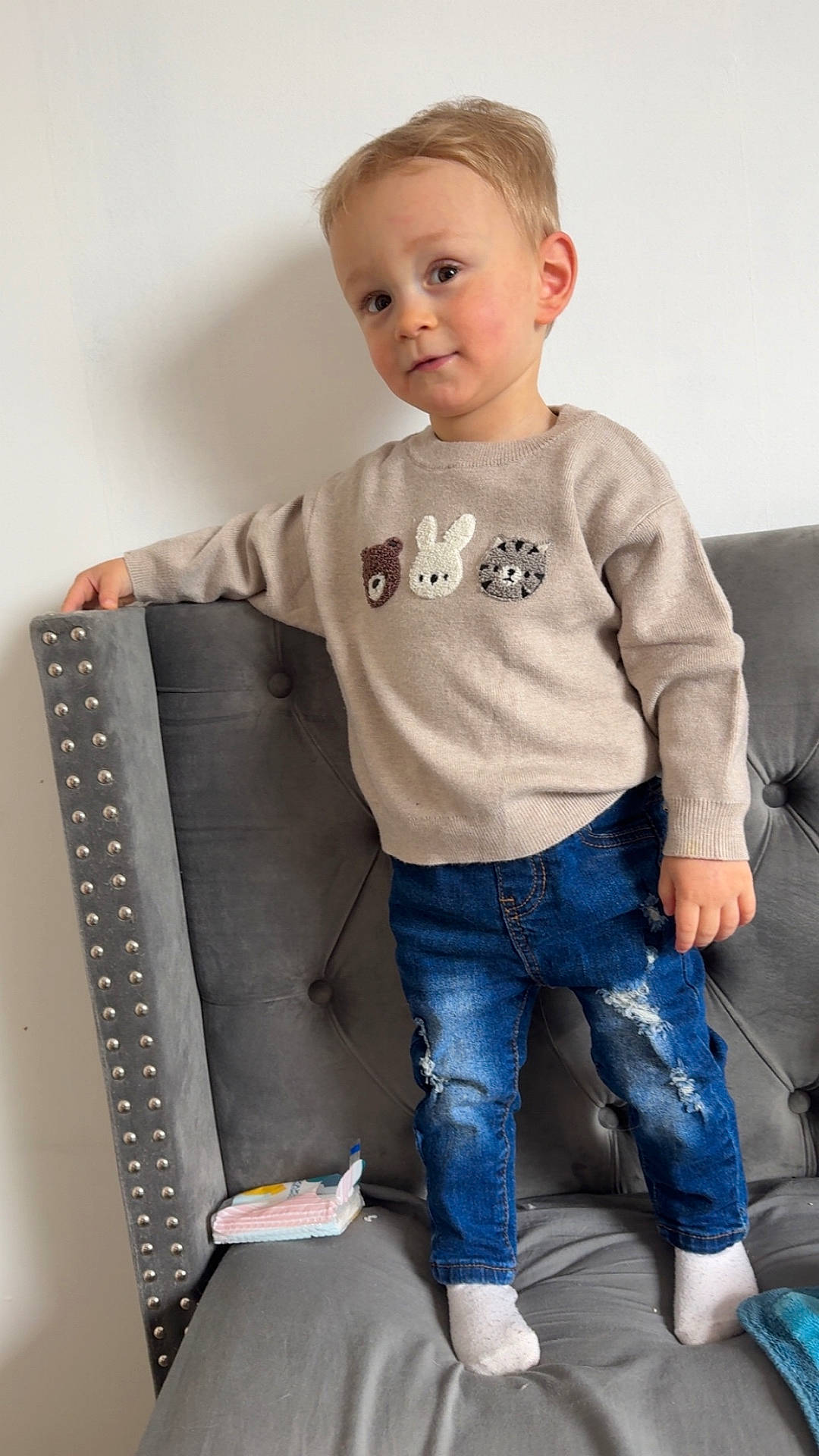Vittorio participe au concours pour gagner de l'argent avec cette photo : casual, child, clothing, couch, cute, furniture, gray, home, indoor, jeans, person, portrait, smiling, socks, sofa, standing, sweater, toddler, wall, young_child