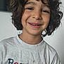background, boy, casual_clothing, child, closeup, colorful, curly_hair, embroidered, face, happy, indoor, light, messy_hair, person, portrait, smiling, textile, tshirt, white_tshirt, young_child