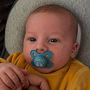 Lyzio a rejoint le concours — aidez-le/la à gagner de superbes lots ! baby, pacifier, hand, yellow_clothing, infant, face, skin, cushion, holding, fingers, comfort, resting, portrait, child, closeup, cute, indoor, soft_texture, calm, adult_hand