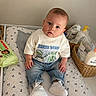 baby, infant, child, jeans, tshirt, sneakers, changing_pad, mickey_mouse_pattern, basket, baby_products, lotion, wipes, indoor, furniture, person, portrait, cute, curious, seated, looking_at_camera