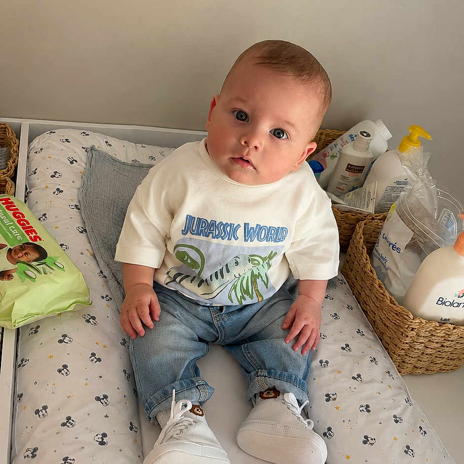 Lyzio a rejoint le concours — aidez-le/la à gagner de superbes lots ! baby, infant, child, jeans, tshirt, sneakers, changing_pad, mickey_mouse_pattern, basket, baby_products, lotion, wipes, indoor, furniture, person, portrait, cute, curious, seated, looking_at_camera