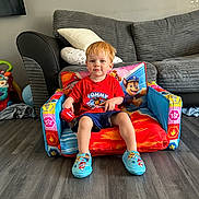 Thomas joined the competition — help win amazing prizes! toddler, child, red_hair, paw_patrol, toy, chair, slippers, red_shirt, blue_shorts, living_room, couch, pillow, floor, wood_floor, indoor, person, smiling, furniture, playtime, cute