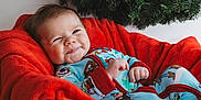 Waylon is registered to the contest to win money with this photo: baby, infant, basket, blanket, red_blanket, wicker, smiling, face, cute, holiday, christmas_wreath, greenery, cozy, indoors, portrait, child, pajamas, blue_pajamas, happy, relaxed