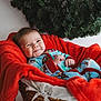 baby, infant, basket, blanket, red_blanket, wicker, smiling, face, cute, holiday, christmas_wreath, greenery, cozy, indoors, portrait, child, pajamas, blue_pajamas, happy, relaxed