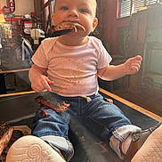 Lucian is registered to the contest to win money with this photo: baby, casual, child, cute, eating, face, food, footwear, hands, indoor, jeans, meat, messy, restaurant, ribs, shoes, sitting, smiling, table, white_shirt