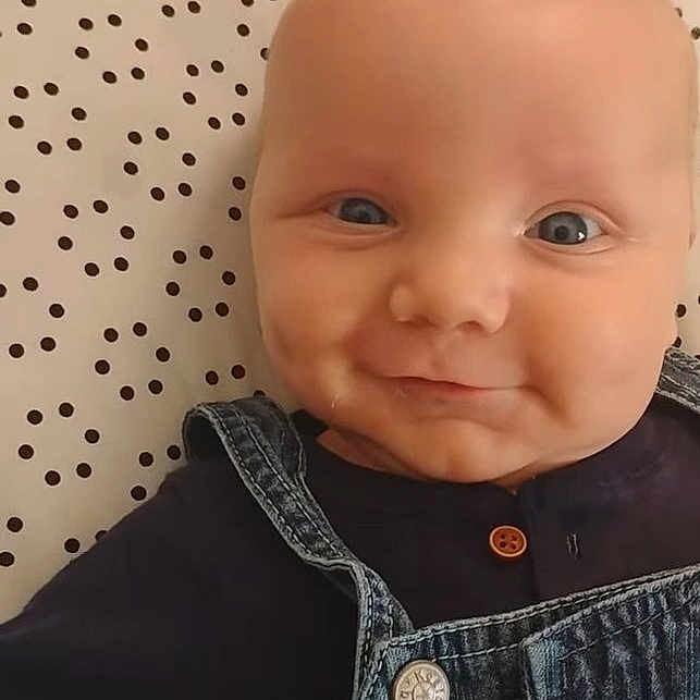 Lincoln is registered to the contest to win money with this photo: baby, infant, smiling, face, denim_overalls, blue_eyes, cute, lying_down, polka_dot_sheet, clothing, child, portrait, cheeks, head, happy, baby_boy, indoors, skin, person, closeup