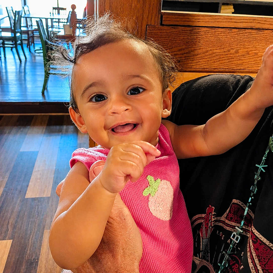 Noorhan is registered to the contest to win money with this photo: adult, arms, baby, baby_teeth, child, curly_hair, family, furniture, happy, held, home, indoors, infant, photography, pink_outfit, portrait, sitting, smiling, strawberry, wooden_floor