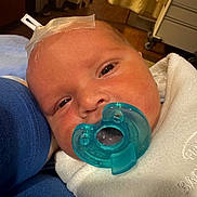 Messiah is registered to the contest to win money with this photo: baby, newborn, pacifier, face, skin, blanket, hospital, medical_tape, infant, person, closeup, resting, blue_sleeve, cute, human, child, indoors, soft, comfort, sleepy