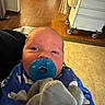Messiah is registered to the contest to win money with this photo: baby, pacifier, blue_blanket, plush_toy, elephant_toy, indoor, floor, wood_floor, tile_floor, medical_cart, curtain, head, face, person, infant, closeup, holding, blanket, cute, child