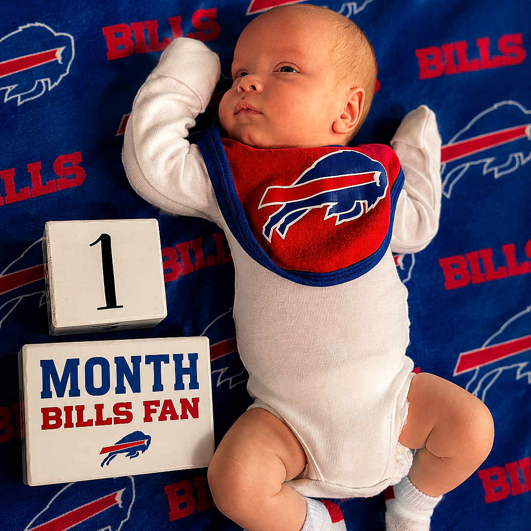 Messiah is registered to the contest to win money with this photo: baby, infant, buffalo_bills, blanket, bib, white_onesie, socks, block_numbers, block_letters, lying_down, milestone, sports_fan, red, blue, white, cute, portrait, indoors, newborn, celebration
