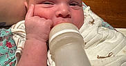 Messiah is registered to the contest to win money with this photo: baby, blanket, bottle, closeup, comfort, cute, expression, face, feeding, hand, indoor, infant, milk, newborn, person, resting, skin, sleepwear, wood, young