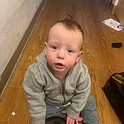 Zeus joined the competition — help win amazing prizes! toddler, child, gray_hoodie, wooden_floor, indoor, person, curious, sitting, floor, casual_clothing, young_child, looking_up, hands, expression, hair, face, eyebrows, skin, indoors, object