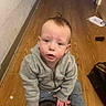 toddler, child, gray_hoodie, wooden_floor, indoor, person, curious, sitting, floor, casual_clothing, young_child, looking_up, hands, expression, hair, face, eyebrows, skin, indoors, object