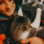 Miles is registered to the contest to win money with this photo: animal, butterfly_filter, camouflage_background, casual, cat, cozy, cute, face, feline, hand, hoodie, indoor, person, pet, portrait, relaxed, smile, tabby_cat, warm, young_person