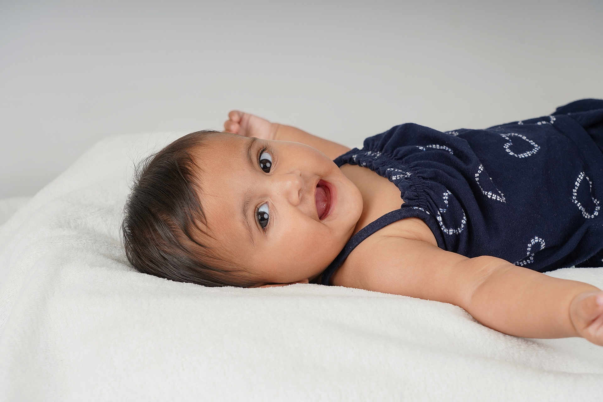 Nikara joined the competition — help win amazing prizes! baby, smiling, lying_down, navy_blue_clothing, white_blanket, infant, happy, portrait, child, face, cute, arms_outstretched, indoors, soft_texture, young_child, one_person, casual_clothing, looking_at_camera, skin, head