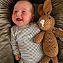 baby, smiling, striped_clothing, crocheted_bunny, plush_cushion, happy, infant, onesie, toy, cute, child, soft_texture, indoor, portrait, small_hand, face, head, cozy, comfort, nestled