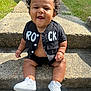 baby, child, smiling, curly_hair, sitting, outdoor, steps, concrete, black_jacket, white_sneakers, happy, cute, sunlight, grass, casual_clothing, portrait, person, infant, small_shoes, daytime