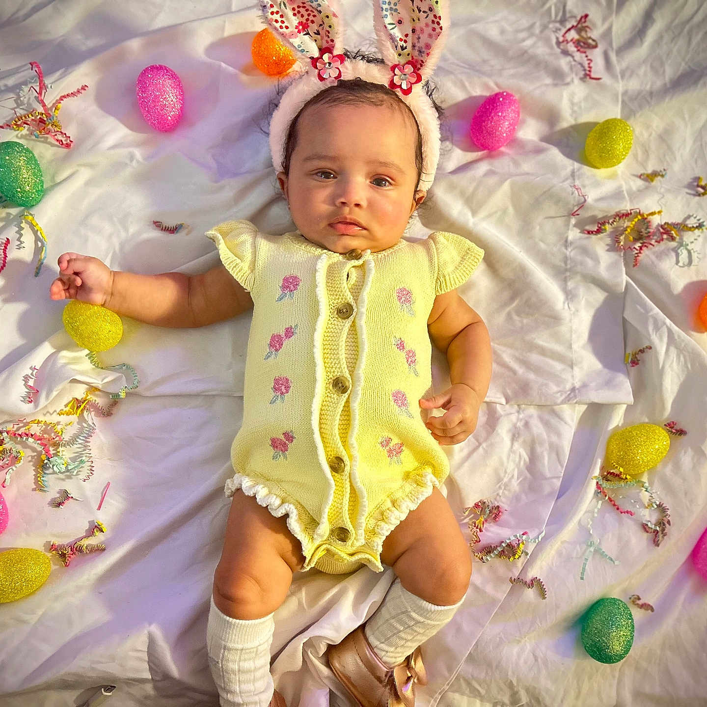 Aubrielle joined the competition — help win amazing prizes! baby, bunny_ears, celebration, child, confetti, cute, easter_eggs, festive, footwear, glitter, headband, indoors, infant, lying_down, pink_flowers, portrait, sock, soft_lighting, white_sheet, yellow_onesie