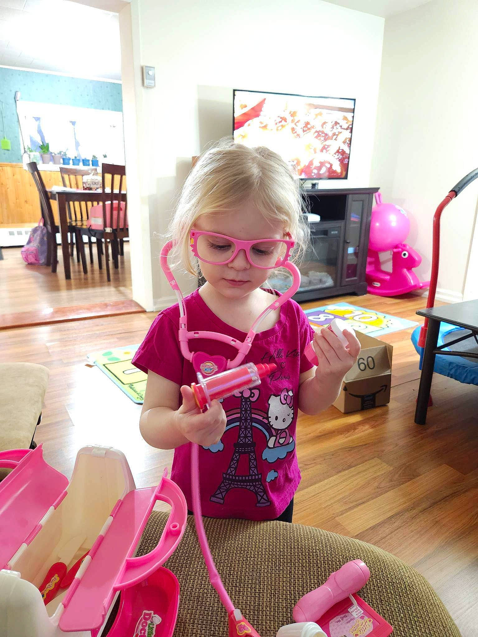 Nova is registered to the contest to win money with this photo: chair, child, comfort, eyewear, flooring, fun, glasses, holiday, human_leg, knee, lap, leisure, magenta, pattern, person, play, room, sitting, thigh, toddler
