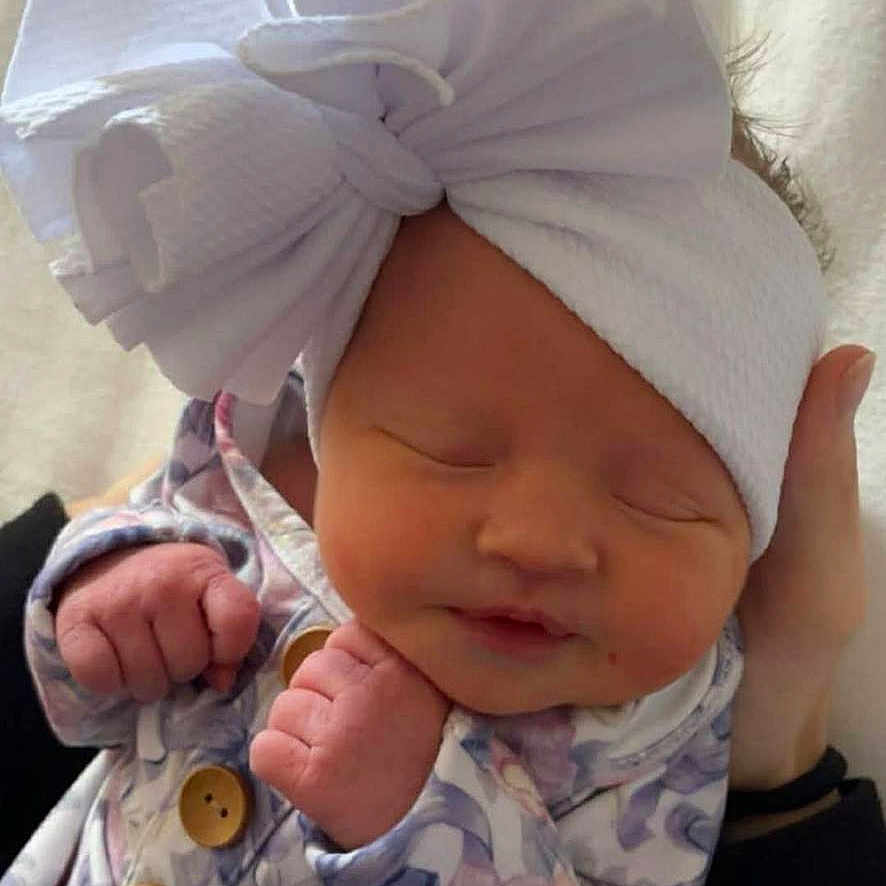 Ensley is registered to the contest to win money with this photo: baby, newborn, infant, sleeping, headband, bow, floral_clothing, cute, peaceful, hand, fist, soft, portrait, child, person, indoor, human, adorable, closeup, resting