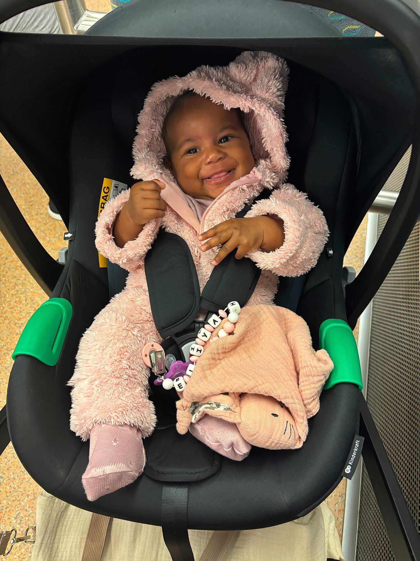 Eliyah a rejoint le concours — aidez-le/la à gagner de superbes lots ! baby, baby_accessories, black_seat, blanket, car_seat, child, cozy, cute, fuzzy_clothing, happy, hooded_jumpsuit, indoors, infant, pacifier, person, pink_onesie, safety_straps, seat, smiling, toy