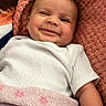 Ameliyah is registered to the contest to win money with this photo: baby, smiling, blanket, infant, cute, lying_down, white_clothing, soft_texture, happy, child, portrait, cheeky_wink, cozy, indoors, pink, orange, young_child, face, skin, person