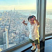 Alexander joined the competition — help win amazing prizes! child, toddler, window, cityscape, skyline, sunset, building, urban, glass, floor, white_shirt, green_shorts, sneakers, smile, happy, indoors, reflection, view, standing, person