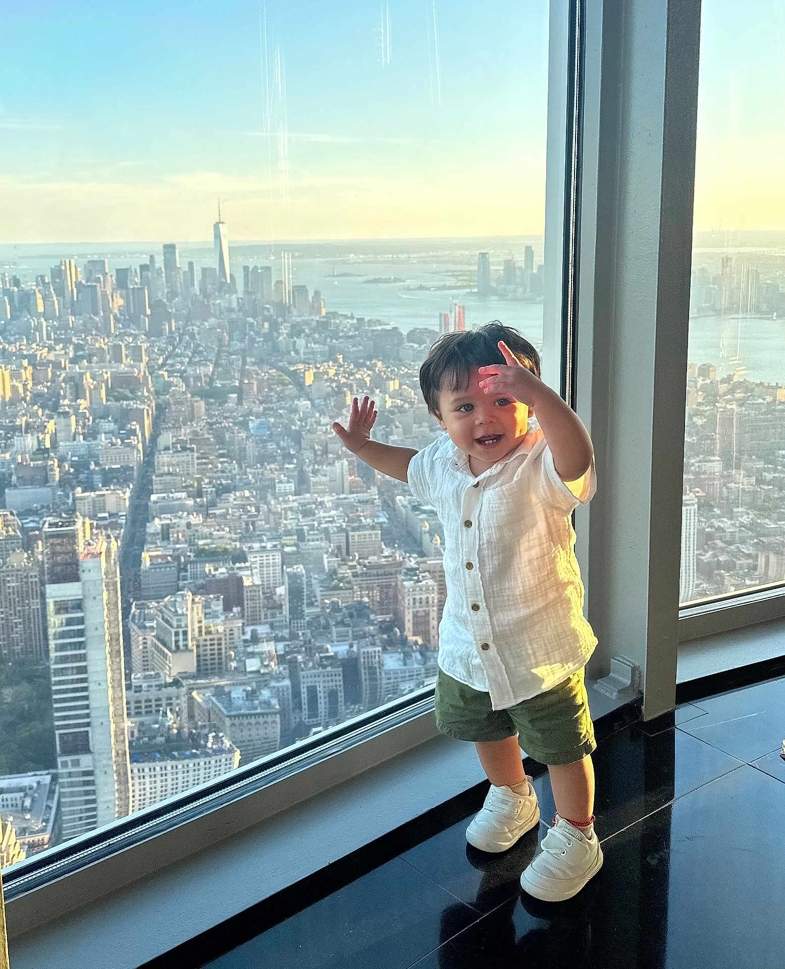 Alexander joined the competition — help win amazing prizes! child, toddler, window, cityscape, skyline, sunset, building, urban, glass, floor, white_shirt, green_shorts, sneakers, smile, happy, indoors, reflection, view, standing, person