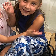 Jade participe au concours pour gagner de l'argent avec cette photo : child, girl, smiling, sitting, bucket, blue_top, patterned_pants, pink_sneakers, hair_tied, indoor, wooden_floor, storage_shelves, containers, hardware_store, happy, casual_clothing, person, young, playful, portrait