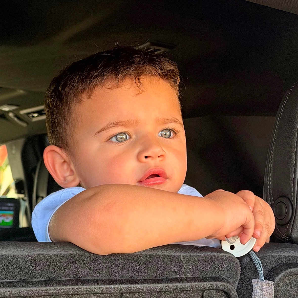 Jayden is registered to the contest to win money with this photo: toddler, child, car_interior, seat, blue_eyes, curious, leaning, young_boy, short_hair, casual_clothing, indoors, daylight, portrait, human_face, expression, hand, car_seat_back, seatbelt, baby_boy, lighting