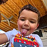 Jayden is registered to the contest to win money with this photo: child, toddler, tongue_out, smiling, white_shirt, flame_design, ceiling_fan, wooden_ceiling, playful, outdoor, window, person, face, short_hair, cute, happy, casual, daylight, expression, closeup