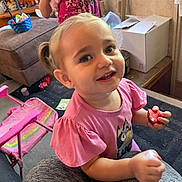 Charli joined the competition — help win amazing prizes! toddler, child, smiling, pink_shirt, pigtails, fruit, indoor, living_room, chair, box, carpet, toy, furniture, person, cute, happy, portrait, casual, playful, home