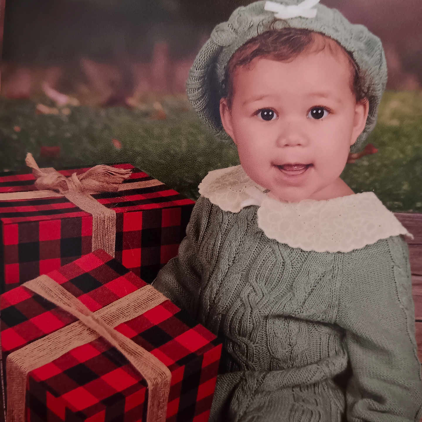 Lillie is registered to the contest to win money with this photo: baby, child, cute, face, festive, gift, green_clothing, happy, hat, holiday, knitwear, outdoor, plaid, portrait, present, seasonal, sitting, smiling, toddler, young_child