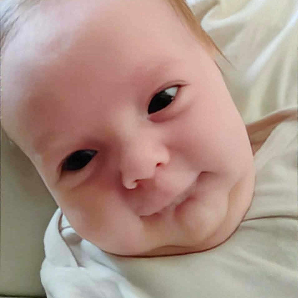 Katheryn is registered to the contest to win money with this photo: baby, blanket, casual, child, chubby_cheeks, closeup, cute, expression, face, hair, head, indoors, infant, lying_down, person, portrait, skin, soft_light, white_clothing, young