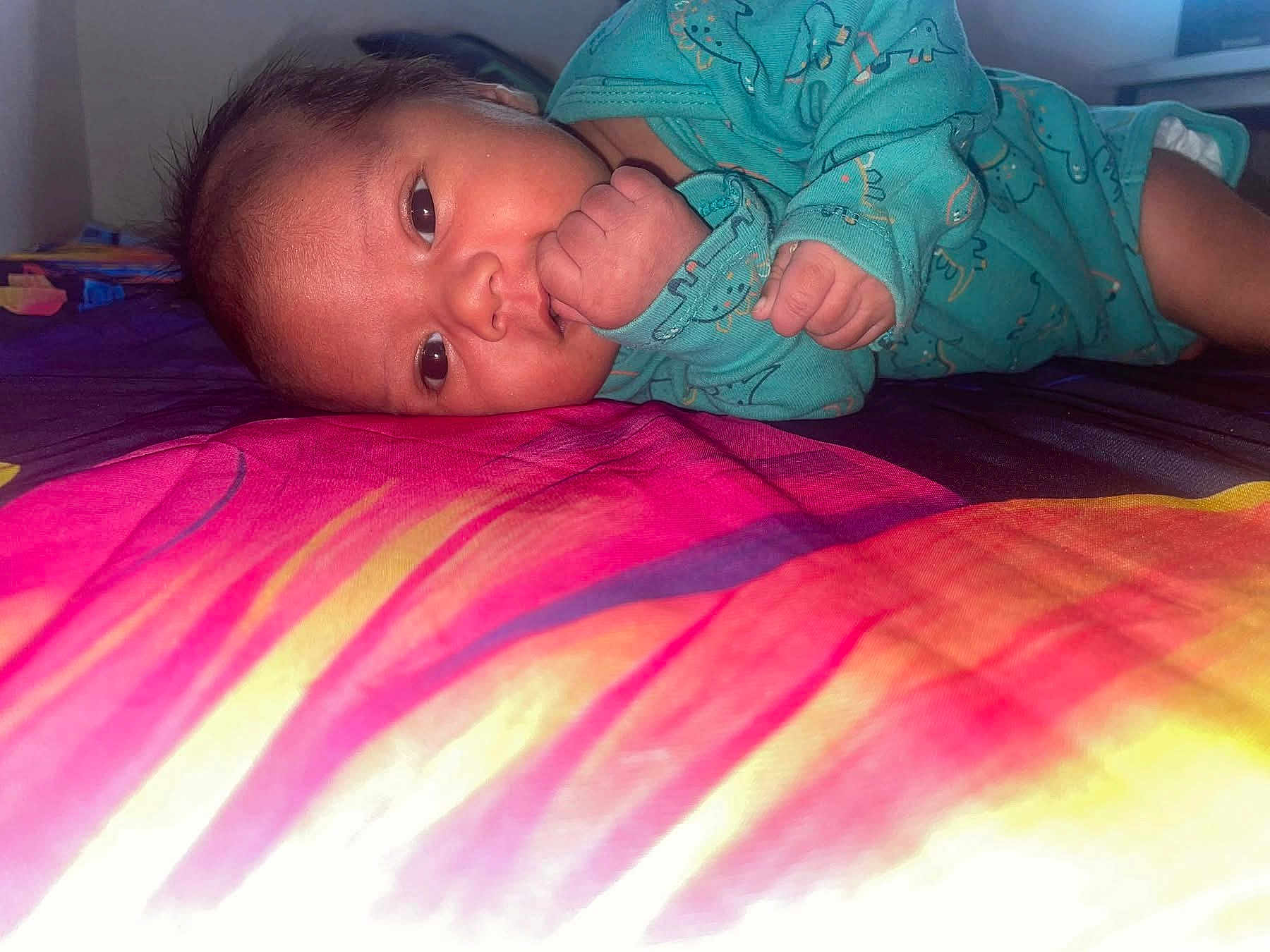 Taoahere participe au concours pour gagner de l'argent avec cette photo : baby, bed, blanket, child, clothing, colorful, cute, dinosaur_pattern, expression, face, hand, head, indoors, infant, lying_down, onesie, portrait, skin, sleepwear, young